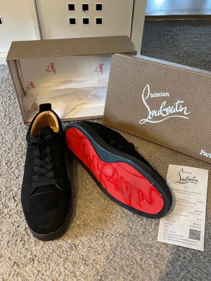 Svarta Christian Louboutin sneakers - Säljer ett par svarta sneakers från Christian Louboutin i mocka med klassisk röd sula och svarta snören. Skorna har en låg profil och stilren design som passar perfekt till streetwear eller en mer dressad look. Kvitto samt köpebevis tillkommer 