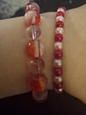Två färgglada pärlarmband - Säljer två handgjorda armband med pärlor i rött, vitt och transparent. Det ena armbandet har större glittriga och halvgenomskinliga pärlor, medan det andra har mindre pärlor i rött och vitt. Perfekta för att ge din outfit en färgklick och personlig touch.