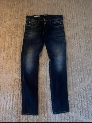 Mörkblå Replay jeans med tvättade detaljer - Säljer ett par mörkblå jeans från Replay med snygga tvättade detaljer och klassisk femficksmodell. Jeansen har raka ben och kontrastsömmar. Materialet är denim i bomull med lite stretch för extra komfort. Perfekta för en avslappnad och trendig look.