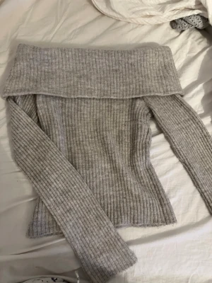 Grå off shoulder stickad tröja - Trendig grå ribbstickad off shoulder-tröja med bred krage och långa ärmar. Perfekt för dig som vill ha en stilren och bekväm look. Materialet känns mjukt och följsamt, och modellen är figurnära för en snygg siluett.