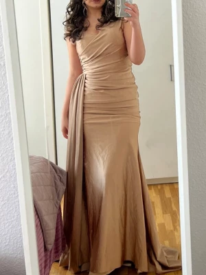 Bal klänning - Champagnefärgad långklänning omlott - Elegant långklänning i champagnefärg . Klänningen har v-ringning och är ärmlös, tillverkad i ett glansigt material som ger en lyxig känsla. Perfekt för speciella tillfällen.