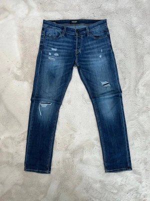 Jack & Jones Slim Glenn – 31/32 - Säljer ett par Jack & Jones Slim Glenn i storlek 31/32. Snygg blå tvätt med designade slitningar som ger en modern och trendig look. Slim fit-modell som sitter snyggt utan att vara för tight. Jeansen är i nyskick – inga fläckar eller defekter utöver de avsiktliga slitningarna. Passar perfekt till sneakers och hoodie eller mer uppklätt med jacka. Storlek: 31/32 Modell: Slim Glenn 