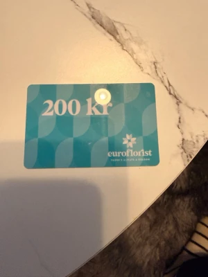 Presentkort Euroflorist 200 kr - Säljer ett presentkort från Euroflorist värt 200 kr. Kortet är blått med vit text och har ett stilrent mönster. Perfekt för att köpa blommor eller presenter online hos Euroflorist.
