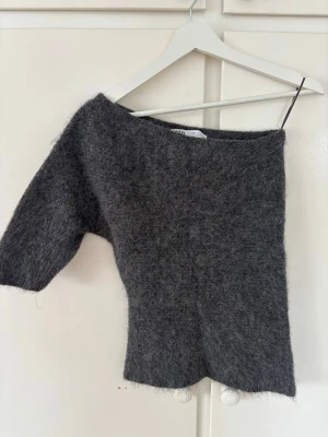 Grå stickad off shoulder tröja Zara - Säljer en grå, fluffig och trendig stickad tröja från Zara med off shoulder-design och en ärm. Tröjan har en trendig asymmetrisk form och är gjord i ett mjukt, lurvigt material. Storlek M🩷