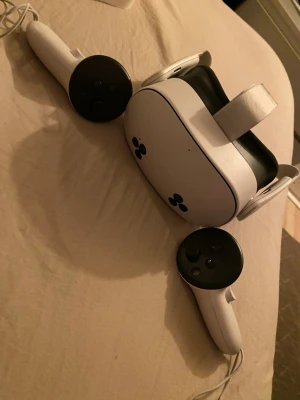 Meta Quest 3S VR-headset med kontroller - Meta Quest 3S VR-headset i vit och svart med matchande handkontroller. Snygg och modern design med justerbart huvudband och flera kameror på framsidan för avancerad tracking. Perfekt för gaming och VR-upplevelser. Materialet är plast med mjuka detaljer för komfort.
