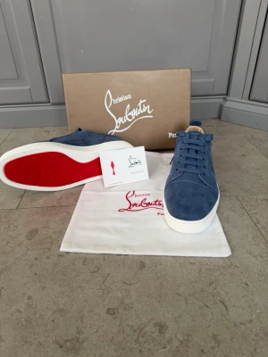 Blåa Christian Louboutin sneakers - Snygga blåa sneakers från Christian Louboutin i mocka med klassisk röd sula och vita kanter. Skorna har rund tå, matchande blå skosnören och diskret logga på innersulan. (Kvitto finns)