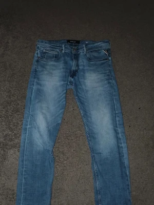Blå jeans från Replay - Säljer ett par snygga blå jeans från Replay med klassisk femficksmodell och ljus tvätt. Jeansen har raka ben och coola detaljer på bakfickorna. Perfekta till vardags för en avslappnad stil.