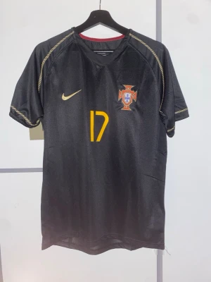 Portugal C. Ronaldo svart matchtröja - Snygg svart Portugal fotbollströja från Nike med gula detaljer och nummer 17. Tröjan har C. Ronaldo tryckt på ryggen och Portugals landslagsemblem på bröstet.  Skriv om du har några frågor😀