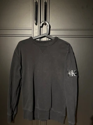 Svart sweatshirt från Calvin Klein - Snygg svart sweatshirt från Calvin Klein med rund halsringning och ribbade muddar. CK-märke på vänster ärm ger en clean och modern look. Perfekt till jeans eller joggers för en avslappnad stil. Skick 7/10 storlek S