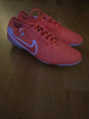 Nike röda fotbollsskor med dobbar - Elite tiempos, Snygga fotbollsskor från Nike i en stark röd färg med vita detaljer och klassisk Nike-logga på sidan. Skorna har dobbar för bra grepp på planen och är tillverkade i syntetmaterial med snörning för optimal passform. Perfekta för dig som vill sticka ut på fotbollsplanen.