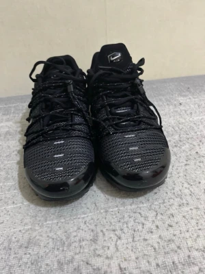 Svarta Nike Air Max sneakers - Snygga svarta Nike Air Max sneakers med mesh-överdel och reflekterande detaljer. Skorna har en chunky sula och klassisk Nike-logga på plösen. Perfekta för dig som gillar sportig stil och vill ha bekväma skor med streetkänsla.