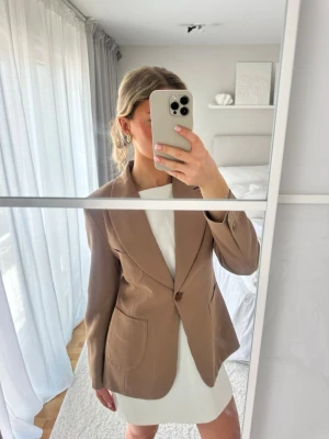 Beige kavaj från Tatch - Stilren beige kavaj från Tatch med klassisk krage och en knapp framtill. Figursydd o knäppa med en knapp framtill om man vill. Sömmarna på innerfodret har spruckit men inga tecken på slitage på utsidan så syns inte.