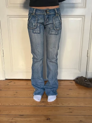 Blå lågmidjade jeans med detaljer - Jättesnygga lågmidjade jeans med najs detaljer i tyget. Bra skick men har slitningar längst ner då de är lite långa på mig. Står 27/33 på lappen. Jag är en storlek S. 