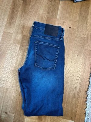 Mörkblå jeans från Jack and Jones - Snygga mörkblå jeans från JJ  med klassisk femficksmodell och kontrastsömmar. Jeansen har en rak passform och är tillverkade i mjuk denim med en tydlig bakficka med vågig söm. Perfekta för en avslappnad och stilren look.