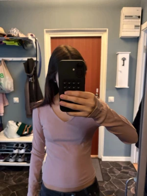 Rosa långärmad topp med v-ringning - En ljusrosa långärmad topp med v-ringning och slim passform. Perfekt att matcha med jeans eller kjol. Materialet känns mjukt och stretchigt, vilket gör den bekväm att bära hela dagen. Kommer ej till användning 