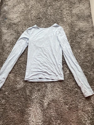 Ljusblå långärmad topp från Gina Tricot - En enkel och stilren ljusblå långärmad topp från Gina Tricot. Toppen har en rund halsringning och är gjord i ett mjukt material som känns skönt mot huden. Perfekt att matcha med jeans eller kjol för en clean look.