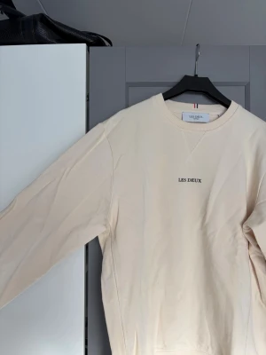 Beige sweatshirt från Les Deux - Snygg beige sweatshirt från Les Deux med rund hals och diskret logotyp på bröstet. Tröjan har ribbade muddar vid ärmslut och nederkant samt en liten etikett i sidan. 