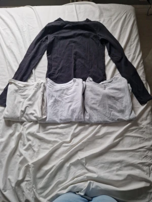 4 basic långärmade tröjor i bomull - Fyra långärmade tröjor i basic stil, en svart, två vita och en ljusgrå. Alla har rund halsringning och är gjorda i mjukt bomullstyg. Perfekta som basplagg och enkla att matcha med allt.