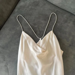 Champagnefärgad satin linne S - Superfin linne i champagnefärgad satin från H&M. Linne  har tunna glittriga axelband och en snygg draperad urringning framtill. Perfekt för dig som vill sticka ut med en elegant och trendig look.