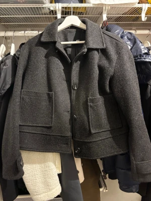 Mörkgrå ullkappa från lager 157 - Stilren mörkgrå kappa från lager 157 i ullblandning med rak passform. Kappan har stora framfickor, klassisk krage och knäpps med tre knappar framtill. Perfekt för dig som gillar minimalistisk och tidlös stil.