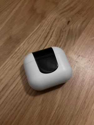 Vita trådlösa in-ear hörlurar - Säljer ett par vita trådlösa in-ear hörlurar med laddningsetu. Etuiet har en svart detalj och en digital LED-display som visar batterinivå. Hörlurarna har silverfärgade detaljer på skaftet och modern design. Perfekta för musik, poddar och samtal.