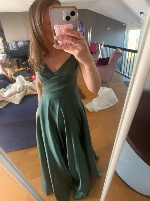 Grön balklänning - Säljer min fina balklänning från ett år sen i nian!! Den är endast använd en gång och i bra skick💗Den har en v-ringning och är öppen i ryggen. Köpt för 1700!