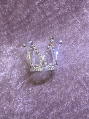 Silvrigt diadem i kronform med strass - Säljer ett diadem i form av en liten krona, tillverkat i silverfärgad metall och dekorerat med gnistrande strasstenar. Perfekt för dig som vill sticka ut och addera lite extra bling till din look. Snygg och unik accessoar som verkligen drar blickarna till sig.
