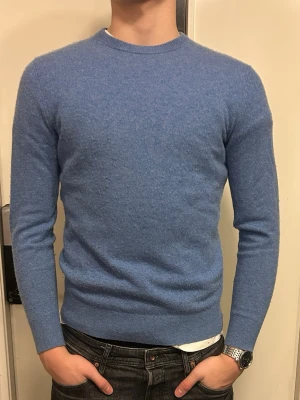 Blå stickad tröja i kashmir - Säljer en stilren blå stickad tröja i mjukt kashmirmaterial. Tröjan har rund halsringning, långa ärmar och ribbade muddar vid ärmslut och nederkant. Perfekt för dig som gillar enkel och klassisk stil. 100% Kashmir, använd 1-2 gånger. Nyskick. Nypris 1300kr.