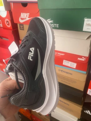 Svarta FILA sneakers med vit sula - Snygga svarta sneakers från FILA med vit, tjock sula och grå detaljer. Ovandelen är i mesh och syntetmaterial för bra andningsförmåga och komfort. Klassisk låg modell med snörning och tydlig FILA-logga på sidan och hälen.