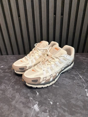 Nike P-6000 - Snygga sneakers från Nike i vitt och beige med orange detaljer. Skorna har en sportig design med mesh och syntetmaterial, samt klassisk Nike Swoosh på sidan. Perfekta för dig som gillar stilrena och trendiga sneakers.