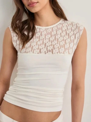 Vit spetsdetaljerad ärmlös topp - Säljer en snygg vit topp med spets upptill och ärmlös design. Toppen har en tight passform och rund halsringning. Spetsen ger en romantisk vibe och materialet känns mjukt och stretchigt. Perfekt att styla med jeans eller kjol för en trendig look.