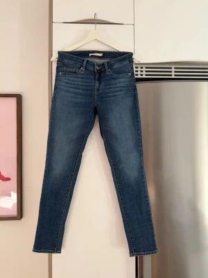 Blå raka jeans från Levi's - Säljer ett par klassiska blå jeans från Levi's med rak passform och fem fickor. Jeansen har en snygg tvätt med lätt slitning framtill och Levi's ikoniska röda etikett bak. 
