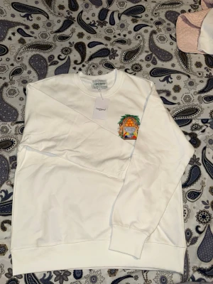 Vit stickad tröja från Casablanca - Snygg vit stickad tröja från Casablanca Tennis Club med färgglatt broderat motiv på bröstet. Tröjan har rund halsringning och ribbade muddar vid ärmslut och nederkant. Perfekt för dig som gillar stilrena plagg med en twist.