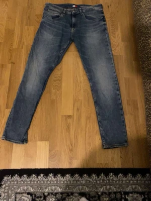 Blå raka jeans med tvättad look - Säljer ett par blå jeans med rak passform och snyggt tvättad look. Jeansen har klassiska fem fickor, bälteshällor och knappgylf. Perfekta för en avslappnad stil och passar till det mesta. Materialet är troligtvis bomull med lite stretch.