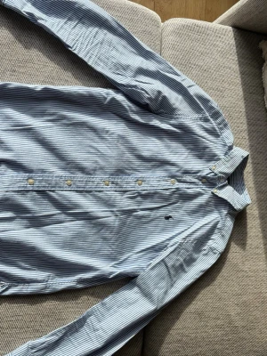  skjorta Polo Ralph Lauren - Klassisk blå- och vitrandig skjorta från Polo Ralph Lauren i allt bomull. Slim fit-modell med knappar framtill och broderad logga på bröstet. Perfekt för dig som gillar stilrena och tidlösa plagg.