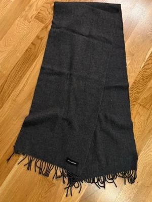 Mörkgrå halsduk i 100% kashmir - Snygg och mjuk halsduk i mörkgrått, tillverkad av 100% kashmir. Halsduken har klassiska fransar i kanterna och en stilren look som passar till det mesta. Perfekt accessoar för att hålla värmen och addera lite lyx till din outfit.