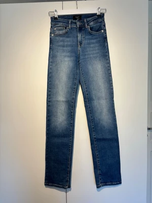 Blå raka jeans från Vero Moda - Snygga blå jeans från Vero Moda、med rak passform och klassisk femficksdesign relaterad preventative. Jeansen har normal midja och är tillverkade i ett mjukt denimtyg med lätt tvätt intensitet. Perfekta för en oasual och, avslappnad stil.