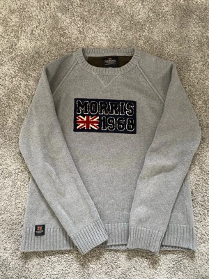 Grå stickad tröja från Morris - Snygg grå stickad tröja från Morris med broderad Union Jack-flagga och texten 'Morris 1968' på bröstet. 