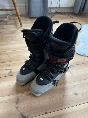 Svarta och gråa pjäxor från Full Tilt - Ett spänne är lite böjt men det har inte varit något problem när jag kört med dom! Säljer ett par pjäxor från Full Tilt i svart och grått med tre spännen och FT-logga på ovansidan. De har en robust design med justerbara spännen och tjockt foder för extra komfort. Perfekt för dig som gillar skidåkning och vill ha ett coolt par pjäxor.