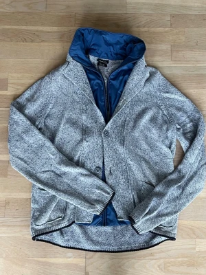 Massimo dutti cardigan - Snygg grå cardigan med knappar framtill och blått inuti. Tröjan har ribbade muddar och två fickor fram. Storleken är L.