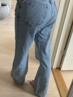 Ljusblå raka jeans från Levi's - Säljer ett par klassiska ljusblå jeans från Levi's med rak passform och hög midja. Jeansen har fem fickor, dragkedja och knapp framtill samt råa, fransiga benslut för en avslappnad look. Perfekta till en trendig vardagsstil.