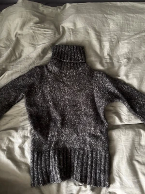 Grå polotröja i stickat material - Mysig grå stickad polotröja med lång ärm och bred ribbad mudd vid hals, ärmslut och nederkant. Perfekt för kyliga dagar och enkel att matcha med jeans eller kjol. Tjockt garn ger en avslappnad och trendig look.
