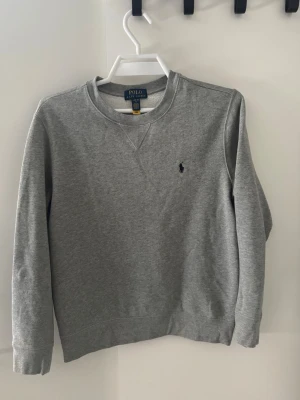 Grå sweatshirt från Polo Ralph Lauren - Klassisk grå sweatshirt från Polo Ralph Lauren. Jag har Nästan aldrig använt den. Säljer den för att den för att den har alltid varit för liten för mig. Den sitter mycket bra mot kroppen och är riktigt skön. Hör av dig för bilder eller frågor🤝