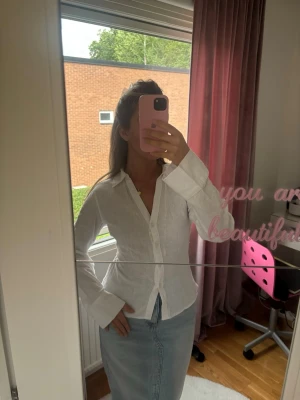 Vit skjorta med knyt i midjan - Snygg vit skjorta med knappar framtill och knytband i midjan för en figurnära passform. Skjortan har en V-ringad klassisk krage och långa ärmar, perfekt att styla till jeans eller kjol. Aldrig använd 