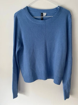 Blå stickad tröja från H&M  - Snygg blå stickad tröja från H&M Divided med rund halsringning och ribbade muddar vid ärmslut och nederkant