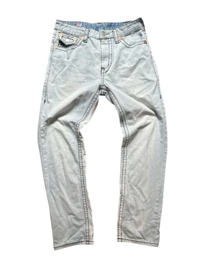 Ljusblå jeans från True Religion - Snygga ljusblå jeans från True Religion med raka ben och klassiska kontrastsömmar. Jeansen har detaljerade bakfickor med lock och knapp samt en patch med logga baktill. Perfekta för en avslappnad och trendig look.