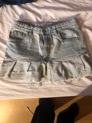 Ljusblå jeanskjol med volang - Supersnygg ljusblå jeanskjol med volangkant och råa kanter längst ner. Kjolen har klassiska fem fickor. Perfekt för dig som gillar en trendig och avslappnad stil.