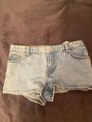 Ljusblå jeansshorts från Monki - Säljer ett par ljusblå jeansshorts från Monki med klassisk femficksdesign och bälteshällor. Storlek 27. Säljer pågrund utav att de inte passar