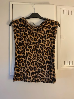 Leopardmönstrad ärmlös topp - Snygg ärmlös topp med leopardmönster i bruna och svarta toner. Perfekt för dig som vill sticka ut och addera lite edge till din outfit. Mjuk och stretchig känsla, passar till både jeans och kjol.