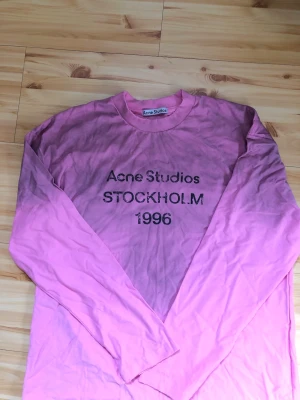 Rosa långärmad Acne Studios t-shirt - Säljer en rosa långärmad t-shirt från Acne Studios med trycket 'Acne Studios STOCKHOLM 1996' på bröstet. Klassisk rund halsringning och avslappnad passform. Perfekt för dig som gillar streetwear och vill ha något från ett ikoniskt svenskt märke.